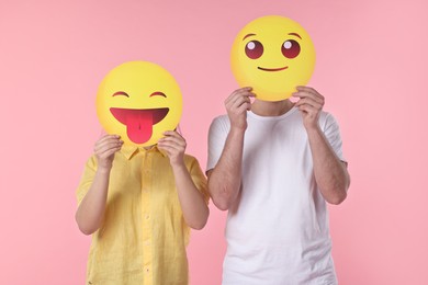 People covering faces with emoticons on pink background