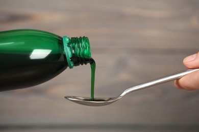 Woman pouring cough syrup into spoon on blurred background, closeup
