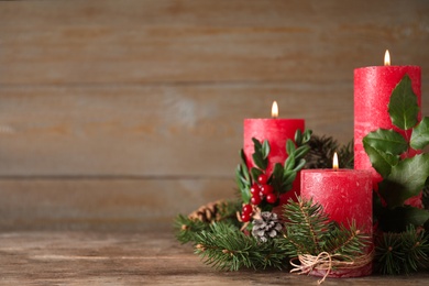 Photo of Burning red candles with Christmas decor on wooden table. Space for text