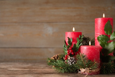 Burning red candles with Christmas decor on wooden table. Space for text