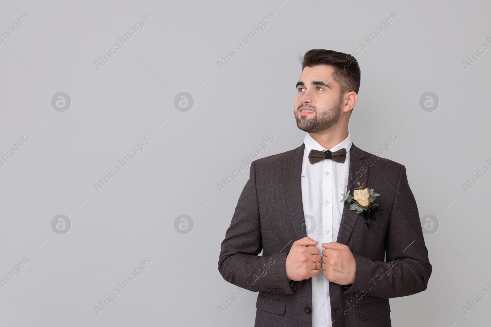 Photo of Handsome young groom with boutonniere on light grey background, space for text. Wedding accessory