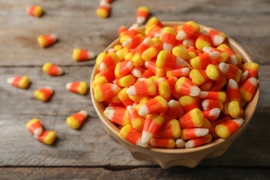 Photo of Bowl with tasty candy corns on wooden table. Space for text