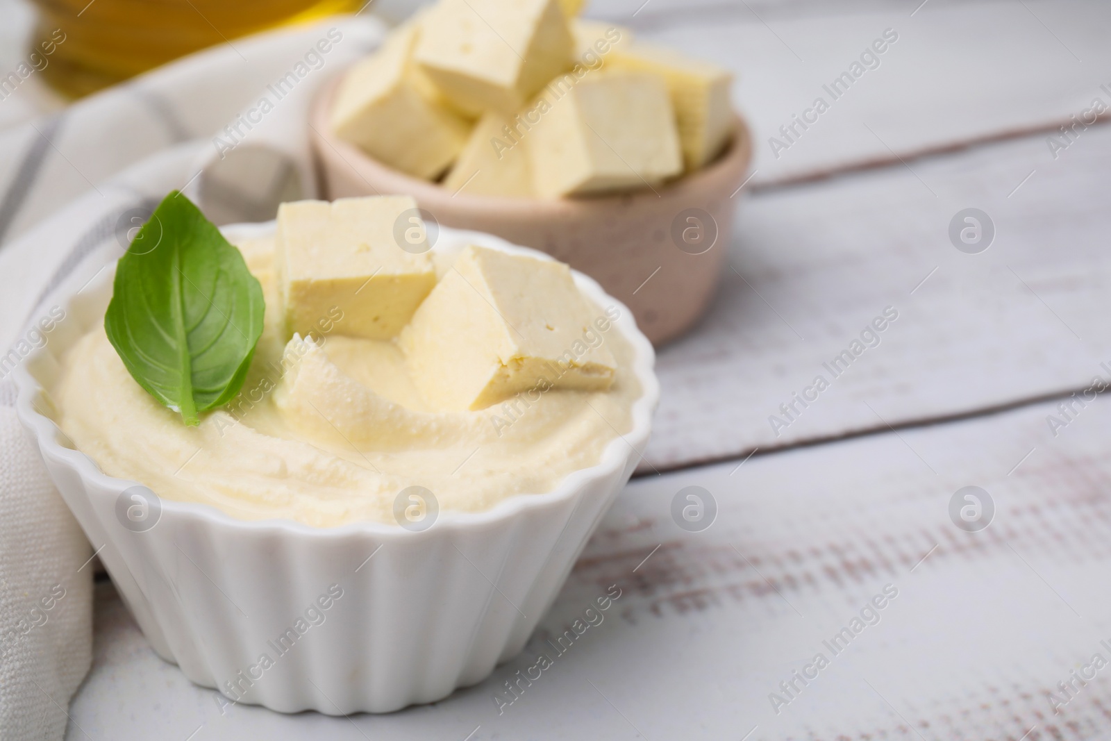 Photo of Delicious tofu sauce and basil leaf on white wooden table, closeup. Space for text