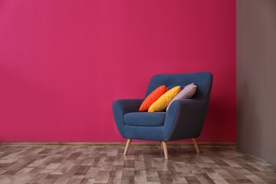 Photo of Armchair with different pillows near color wall in room