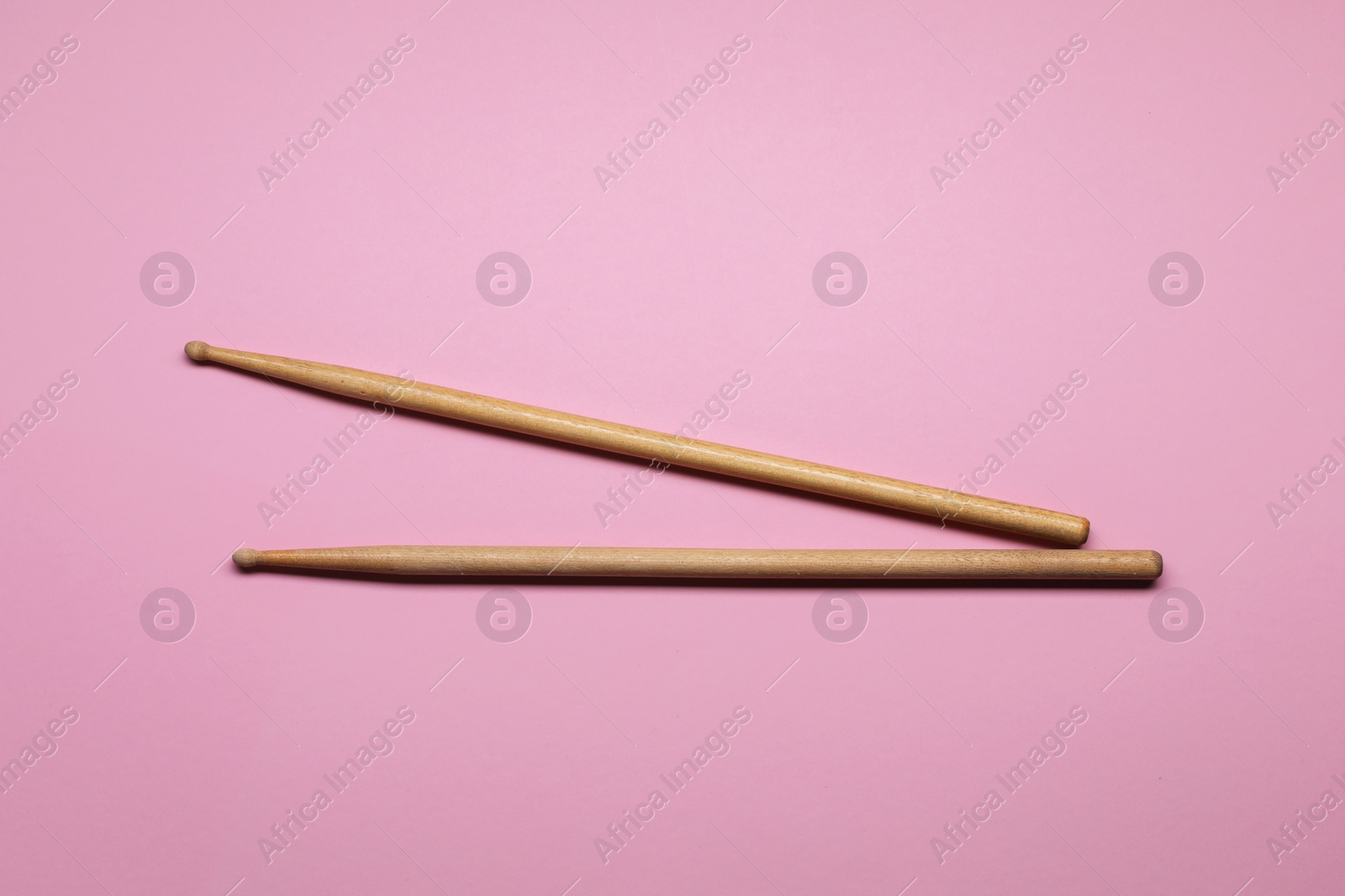 Photo of Two wooden drum sticks on pink background, top view