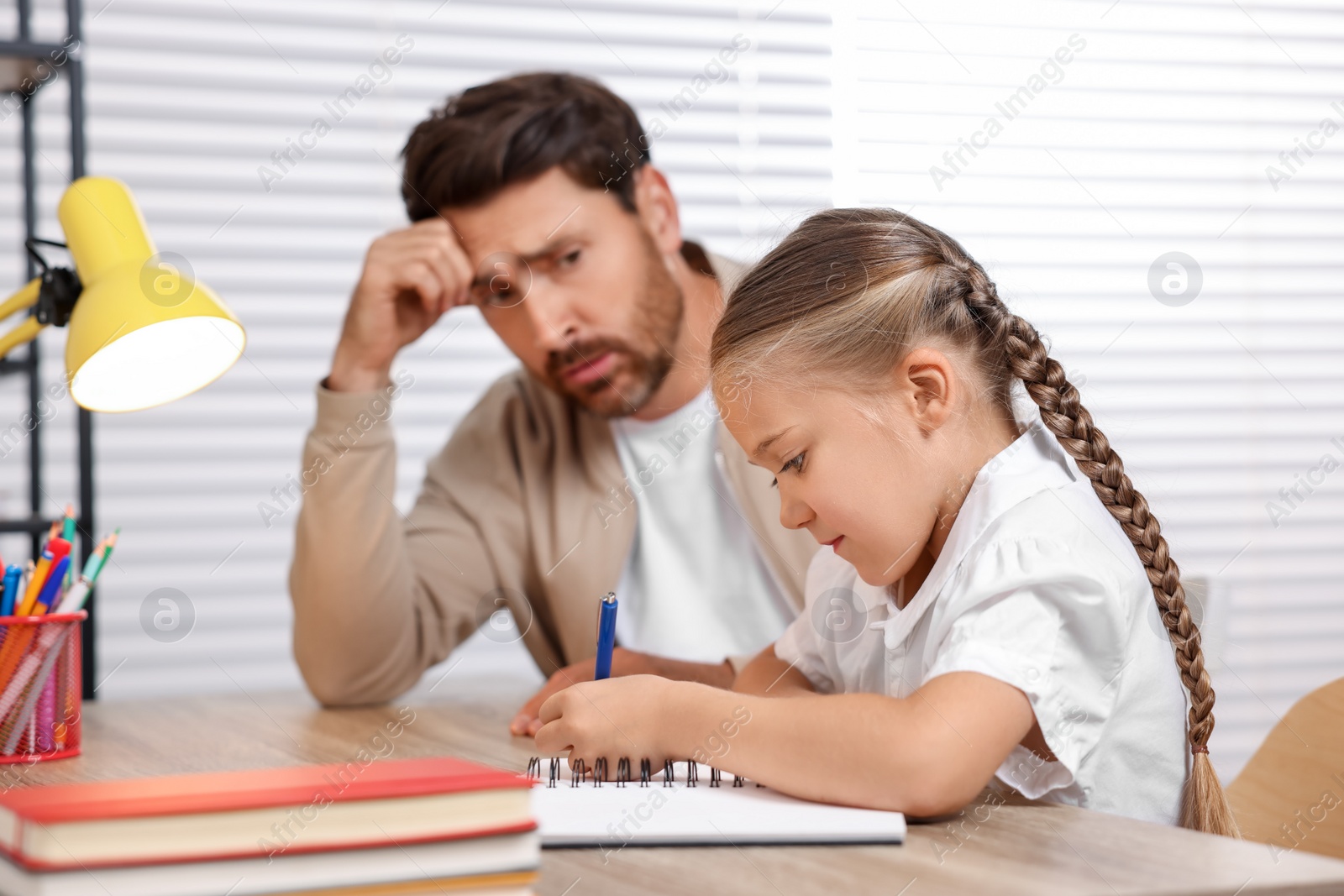 Photo of Dyslexia problem. Annoyed father helping daughter with homework at table indoors, selective focus