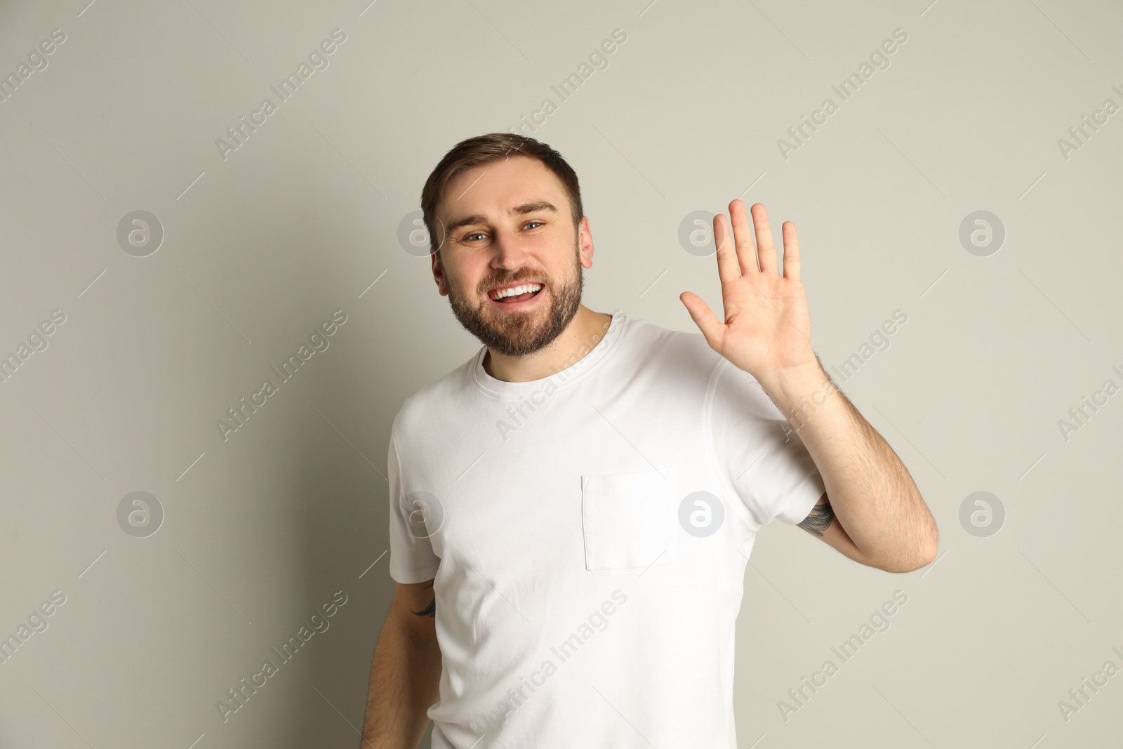 Photo of Happy young man waving to say hello on light grey background