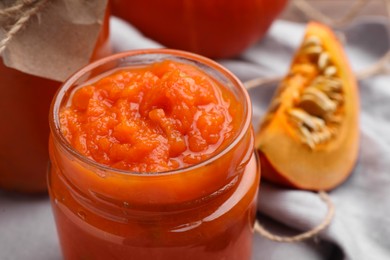 Photo of Jar of pumpkin jam and fresh pumpkin on cloth, closeup