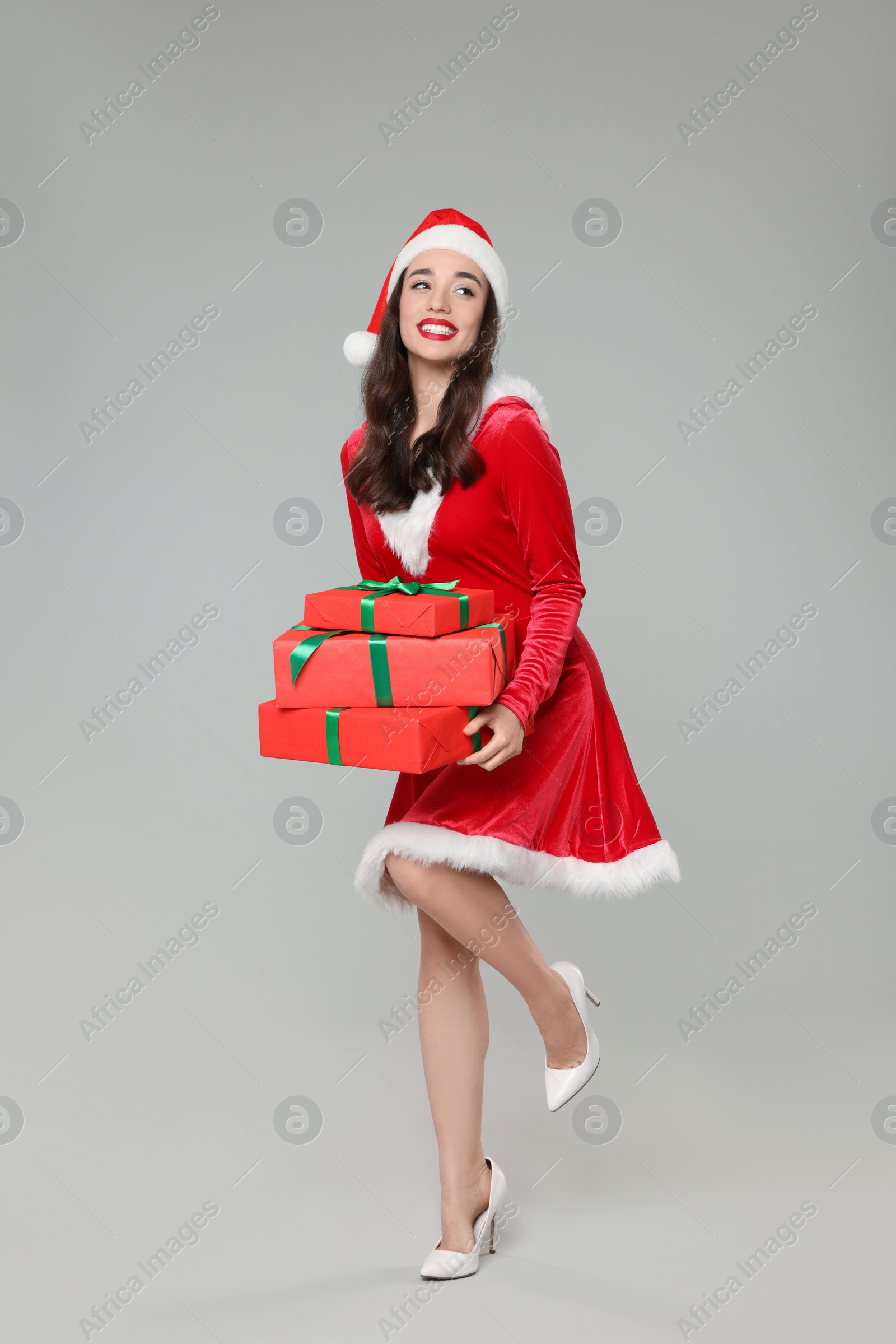 Photo of Beautiful young woman in red dress and Santa hat with Christmas gifts on grey background