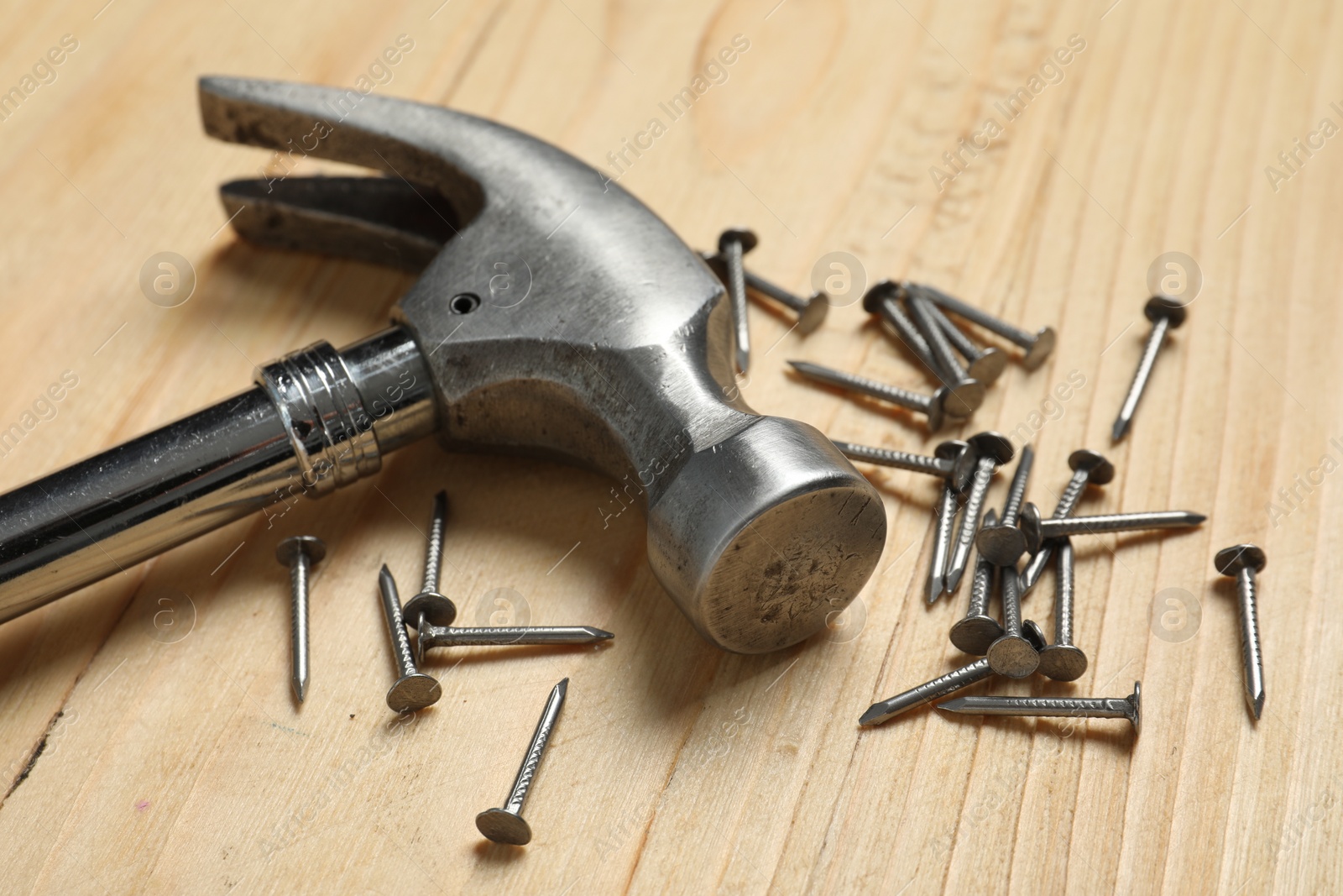 Photo of New hammer and metal nails on wooden table, closeup. Professional construction tool