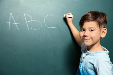 Photo of Little child writing letters on green blackboard. Space for text