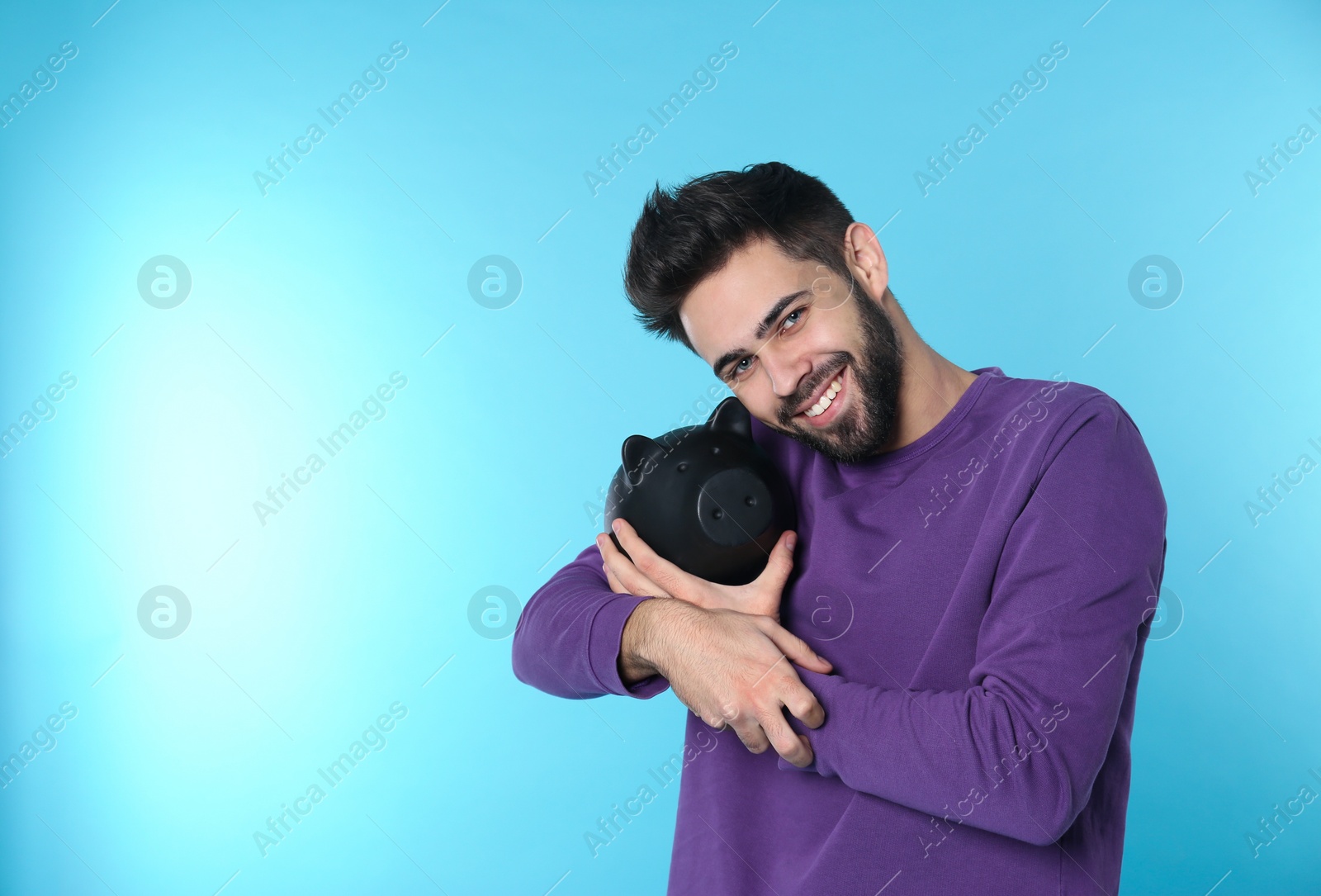 Photo of Happy young man with piggy bank and space for text on color background. Money saving