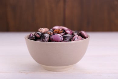 Photo of Bowl with dry kidney beans on white wooden table, closeup