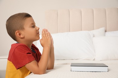 Photo of Cute little boy with hands clasped together saying bedtime prayer over Bible at home. Space for text