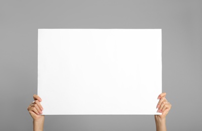 Photo of Woman holding white blank poster on grey background, closeup. Mockup for design