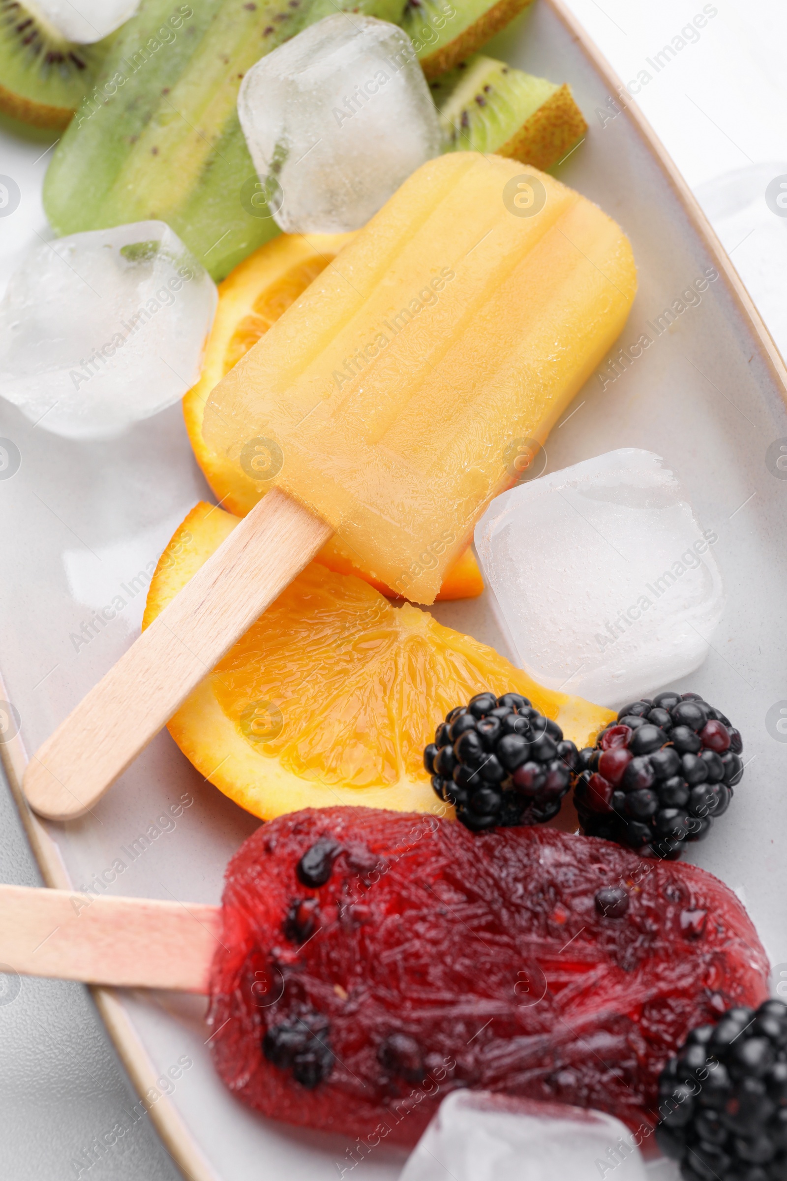 Photo of Delicious popsicle, ice cubes and fresh fruits on plate, closeup