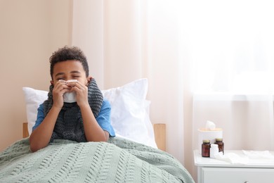 African American boy with scarf and tissue blowing nose in bed indoors, space for text. Cold symptoms