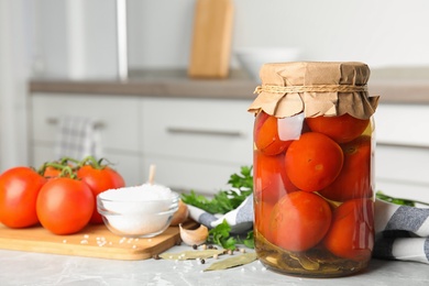 Jar with pickled tomatoes and vegetables on grey table in kitchen. Space for text
