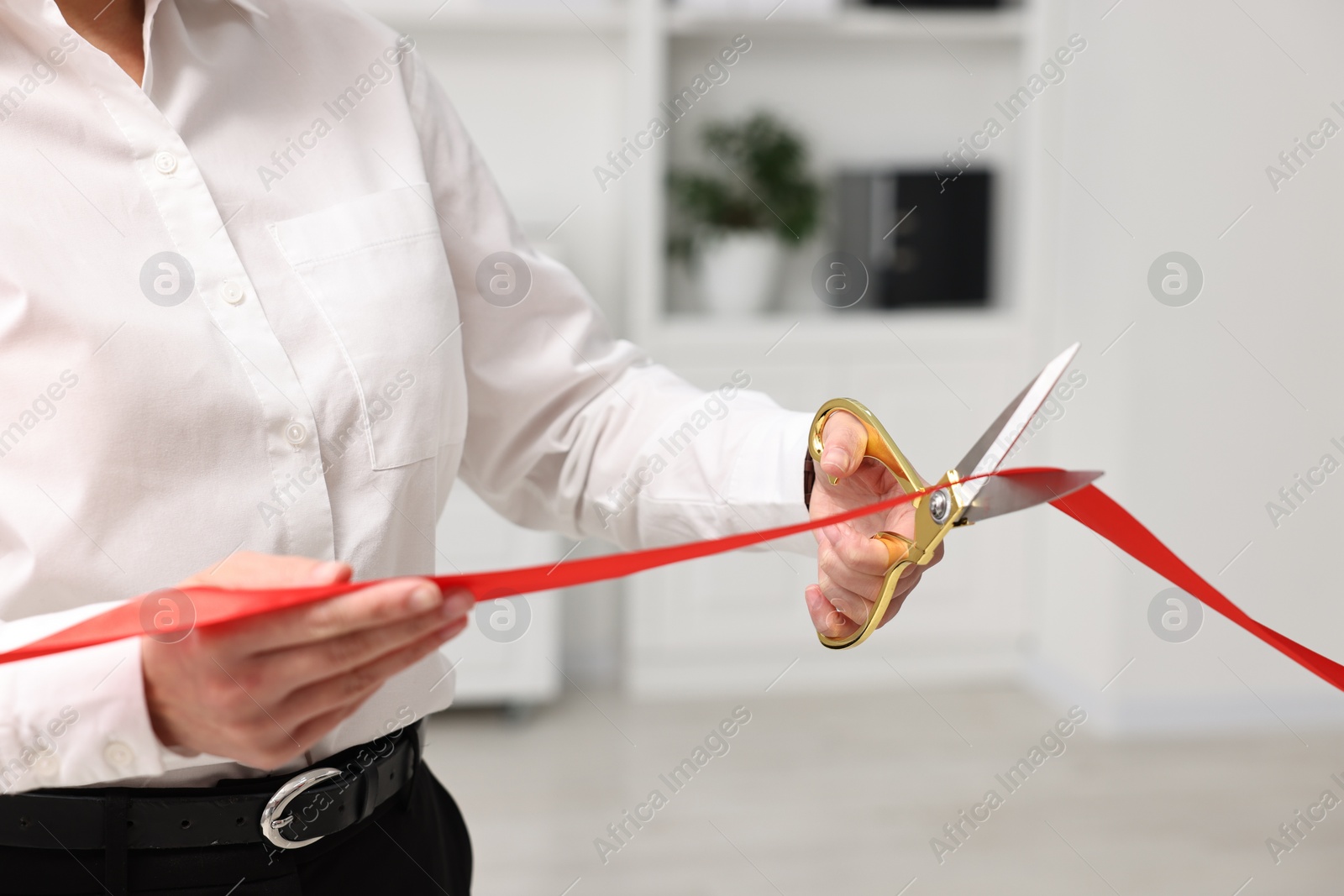 Photo of Woman cutting red ribbon with scissors indoors, closeup