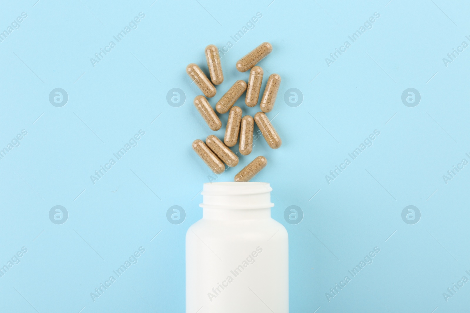 Photo of Bottle and vitamin capsules on light blue background, top view