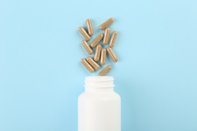 Bottle and vitamin capsules on light blue background, top view