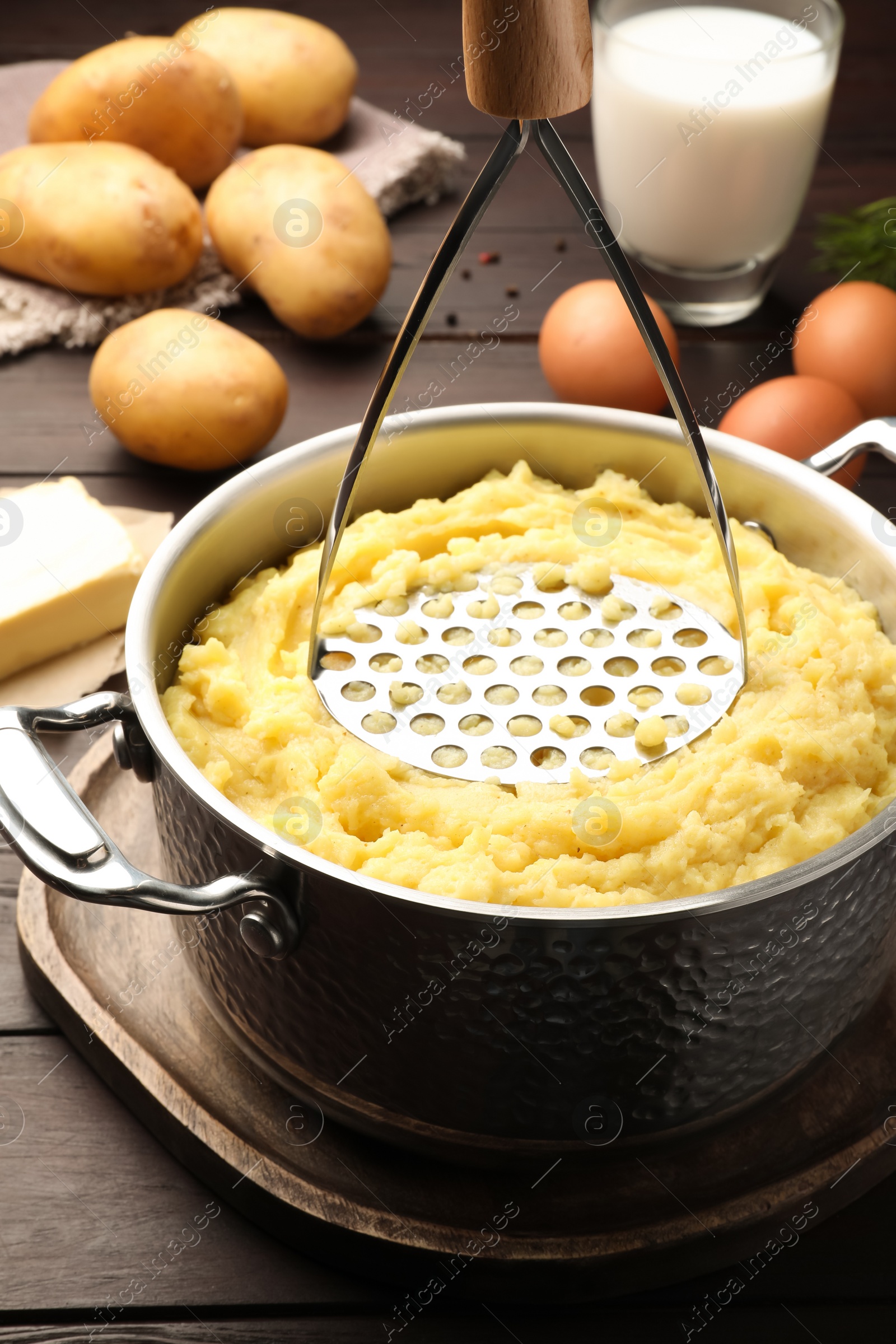 Photo of Mashing potatoes in pot on wooden table
