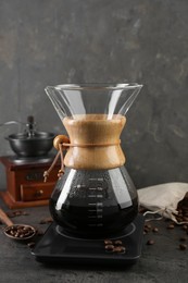 Photo of Making drip coffee. Glass chemex coffeemaker, beans and scales on gray table