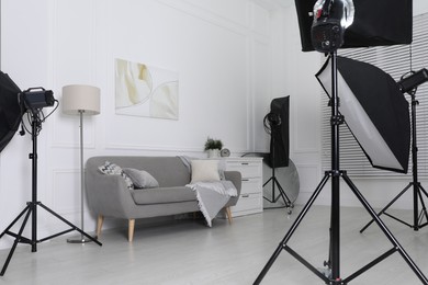 Set of stylish furniture surrounded by professional lighting equipment in photo studio. Cozy living room interior imitation