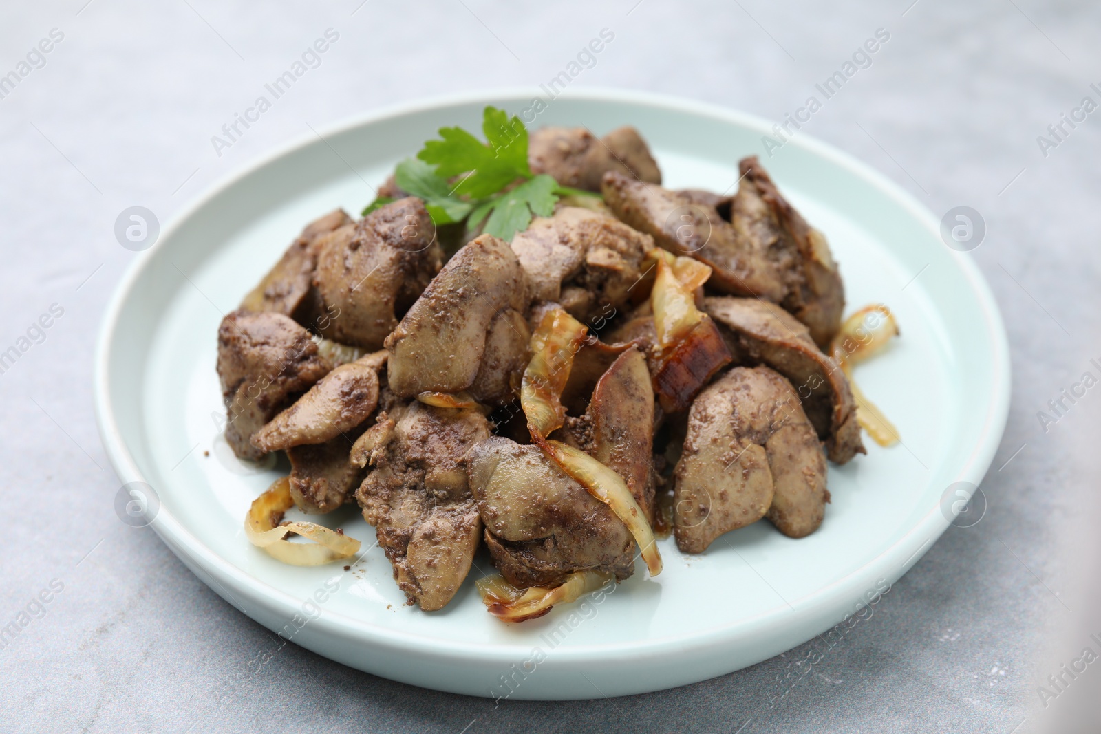 Photo of Tasty fried chicken liver with onion and parsley on grey table, closeup