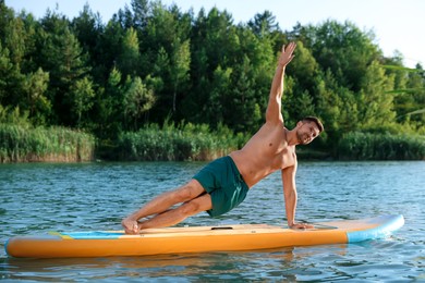 Man practicing yoga on color SUP board on river