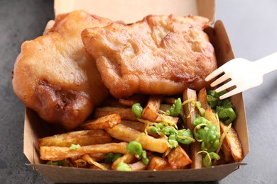 Photo of Tasty fish, chips and peas in paper box on grey table, above view