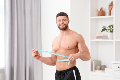 Photo of Portrait of happy athletic man measuring waist with tape at home. Weight loss concept