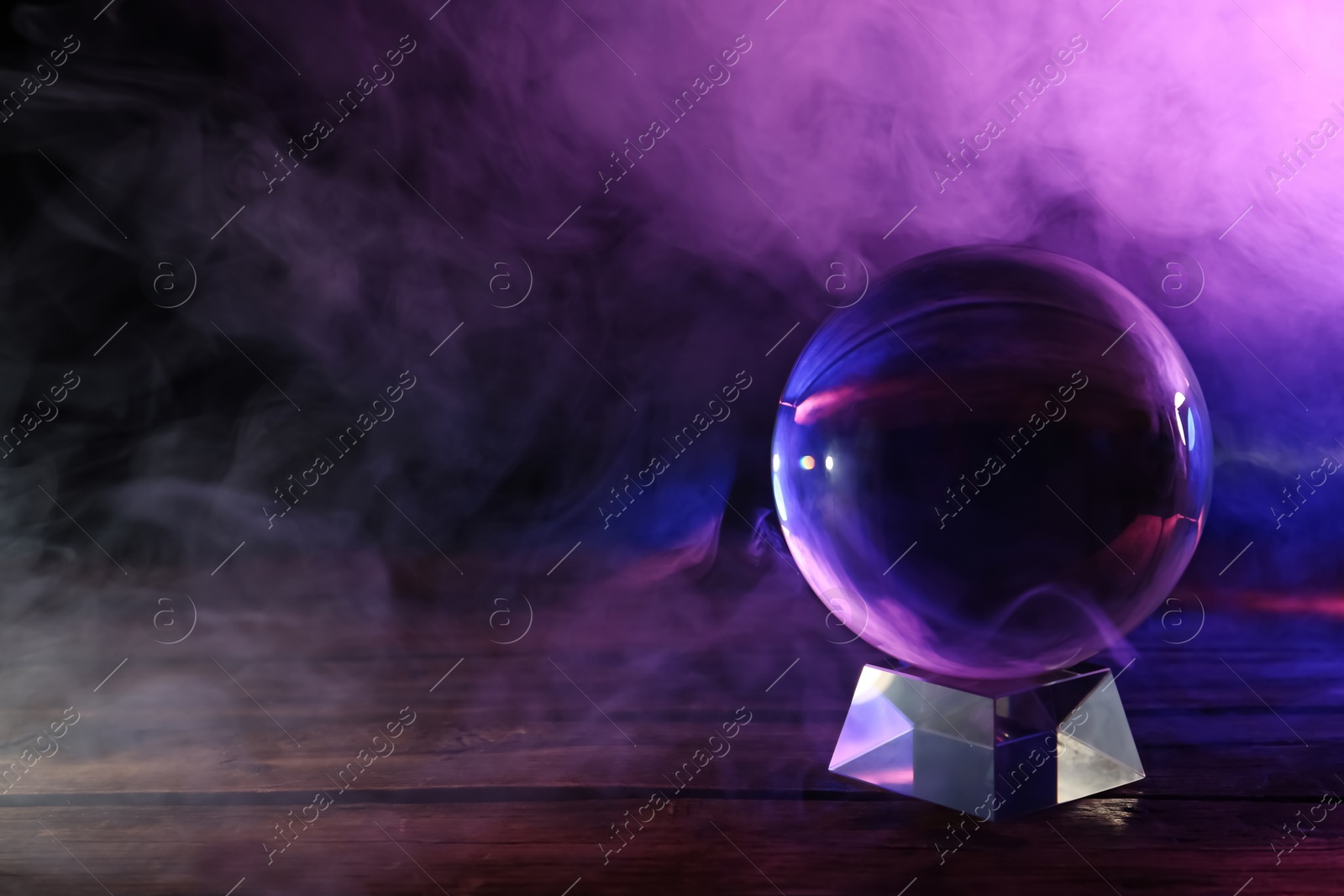 Photo of Crystal ball on table and smoke against dark background, space for text. Predictions of future