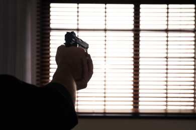 Photo of Man holding gun indoors, closeup. Space for text
