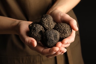 Photo of Woman holding heap of truffles in hands on black background, closeup