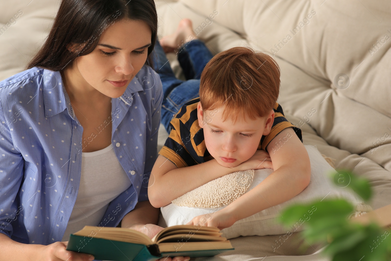 Photo of Mother reading book with her son in living room at home