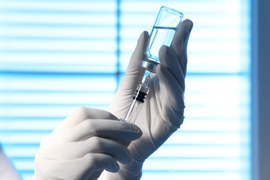 Photo of Woman filling syringe with vaccine from vial on blurred background, closeup