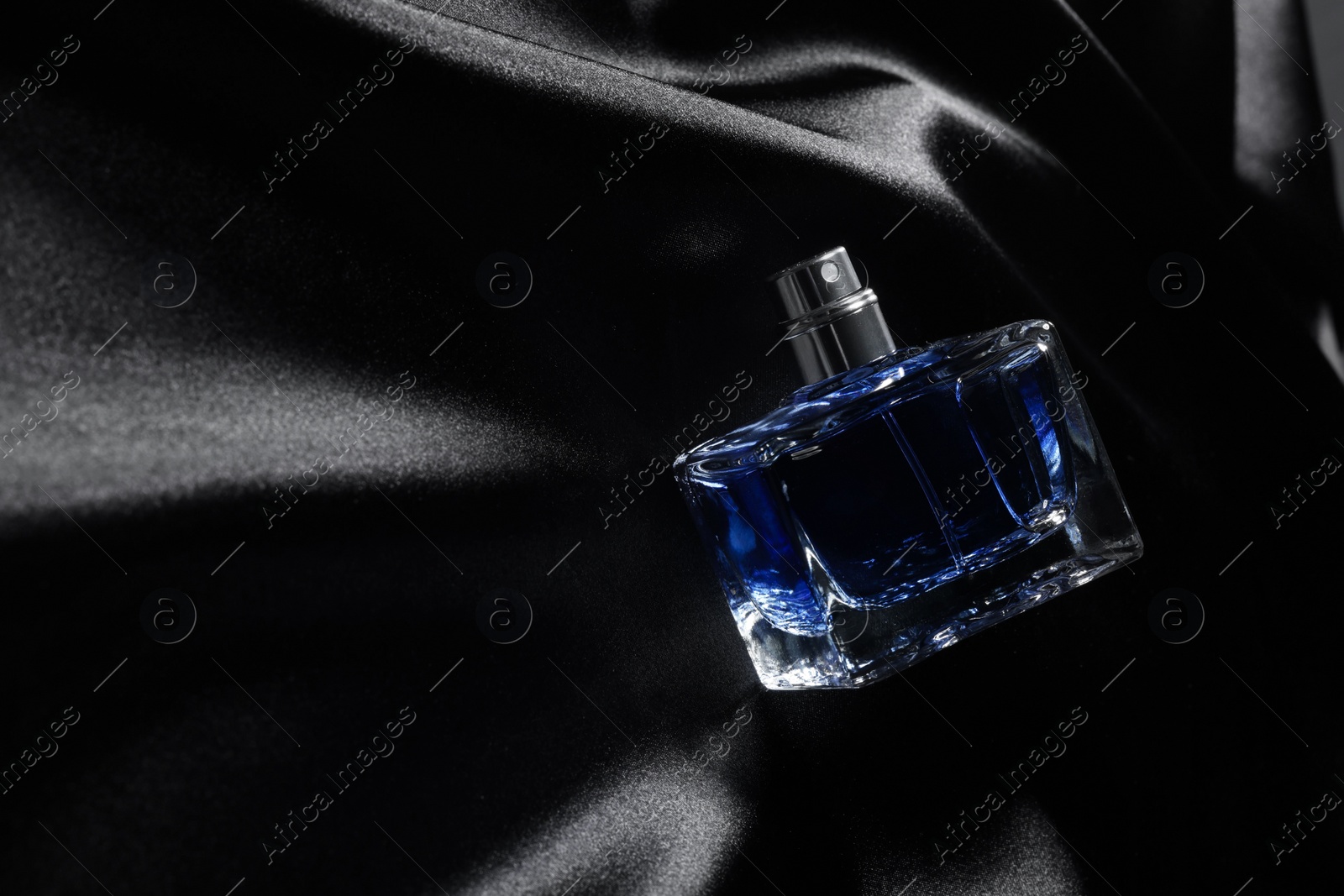 Photo of Luxury men's perfume in bottle on black satin fabric, top view. Space for text