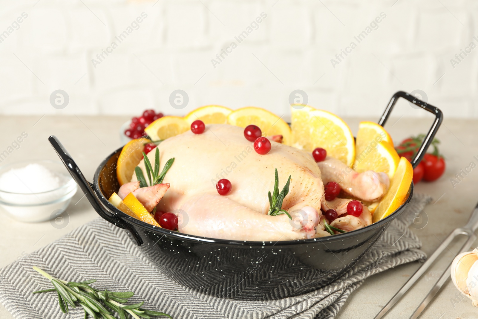 Photo of Chicken with orange slices, red berries and rosemary in round baking pan on light grey table