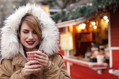 Woman with cup of mulled wine at winter fair. Space for text