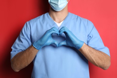 Photo of Doctor making heart with hands on red background, closeup