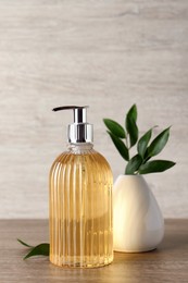 Stylish dispenser with liquid soap and green leaves in vase on wooden table