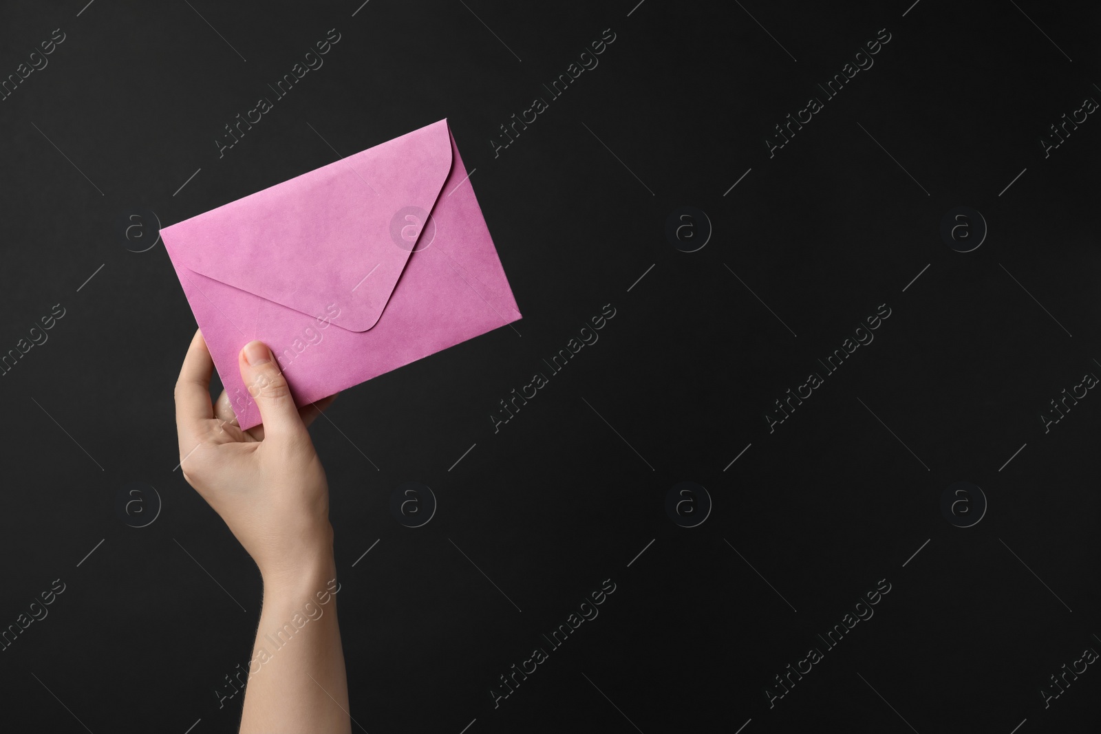 Photo of Woman holding pink paper envelope on black background, closeup. Space for text