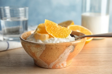 Photo of Creamy rice pudding with orange slices in bowl on wooden table