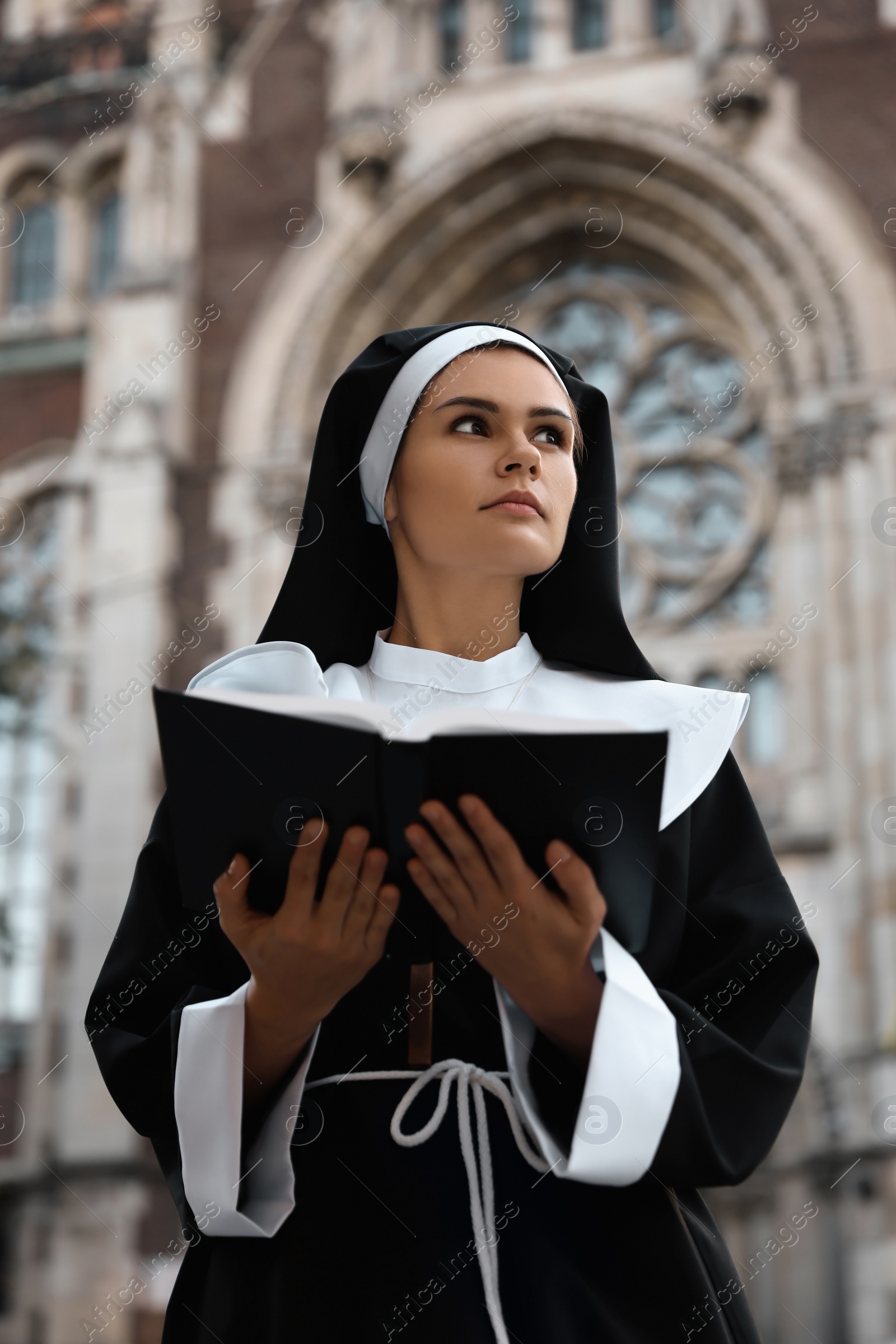 Photo of Young nun reading Bible near cathedral outdoors