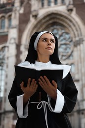 Young nun reading Bible near cathedral outdoors