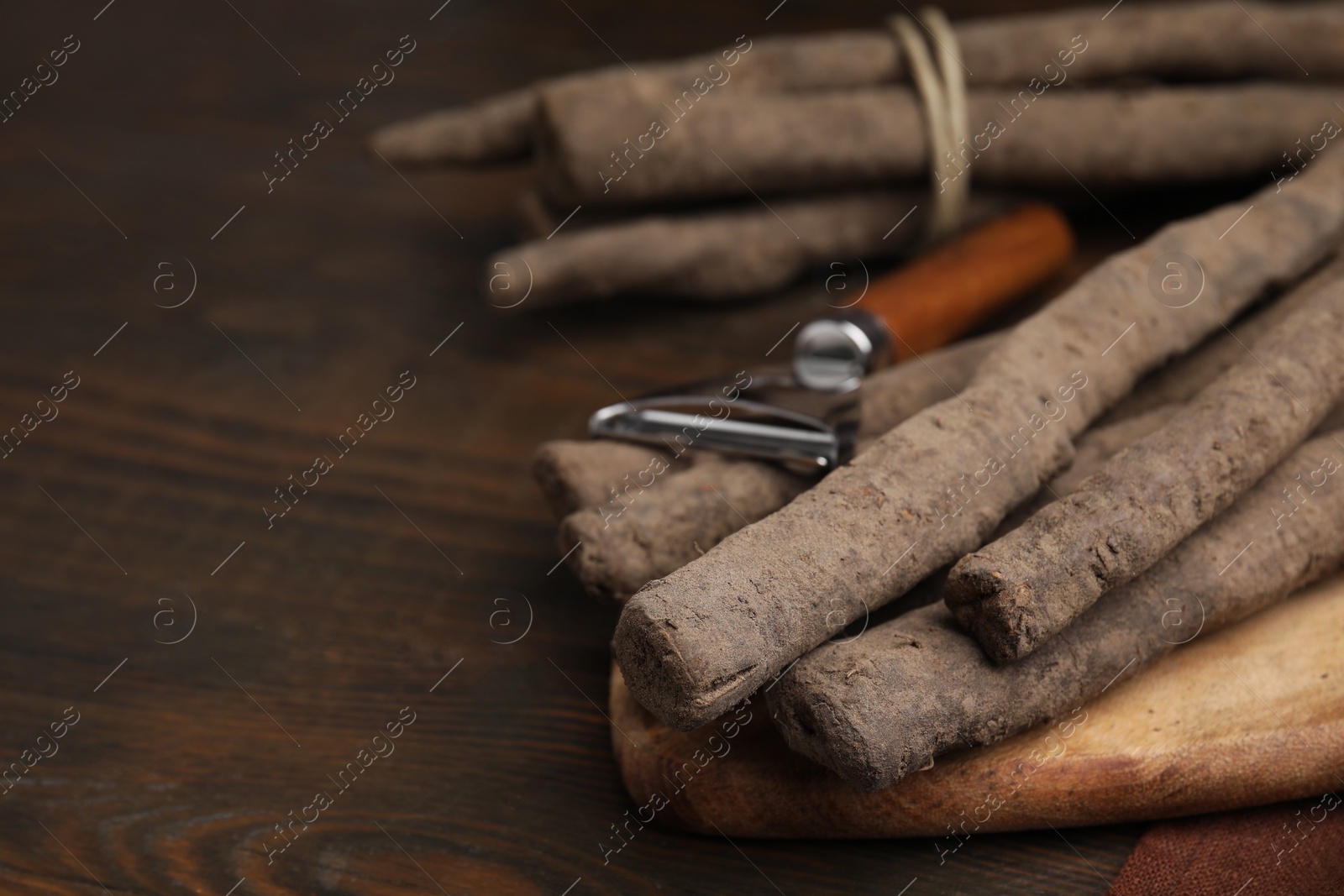 Photo of Raw salsify roots and peeler on wooden table, closeup. Space for text