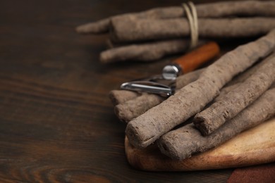 Photo of Raw salsify roots and peeler on wooden table, closeup. Space for text