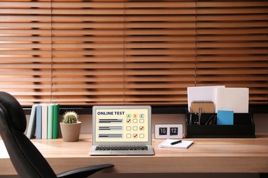 Laptop with online test on wooden desk in office