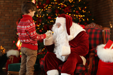 Little boy treating Santa Claus with cookies near Christmas tree indoors